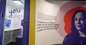 A photograph of an interior wall in the People of Hope Museum that features a photograph of a storyteller and information about the Catholic Charities network's services to people in need across the country.
